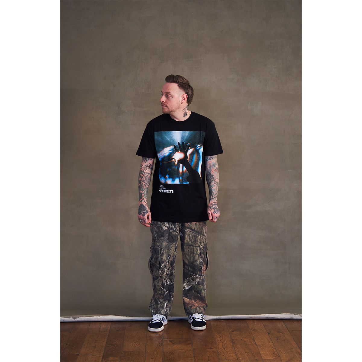 Sam Carter wearing a black crew neck t-shirt with The Sky, The Earth and All between album artwork across the front.