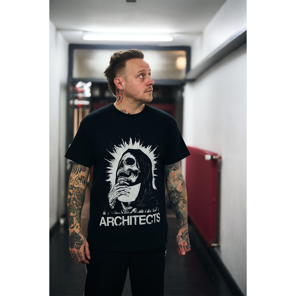 Man wearing a black unisex short-sleeve t-shirt featuring a vintage-style skull graphic and vintage looking text reading ‘Architects’ across the front